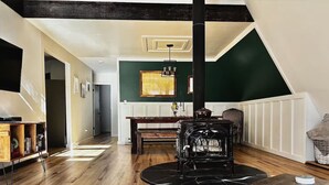 Un salon chaleureux avec un plancher en bois, un poêle noir, une bibliothèque et un tableau accroché au mur.
