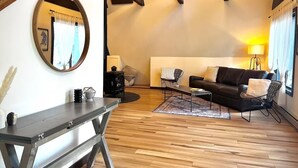 Un salon chaleureux avec un plancher en bois, un canapé noir, une table basse, une cheminée et un miroir rond.