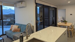 Une cuisine moderne équipée d’un évier, un coin repas avec une table et des chaises, un canapé avec des coussins et une vue sur l’extérieur à travers une porte vitrée.