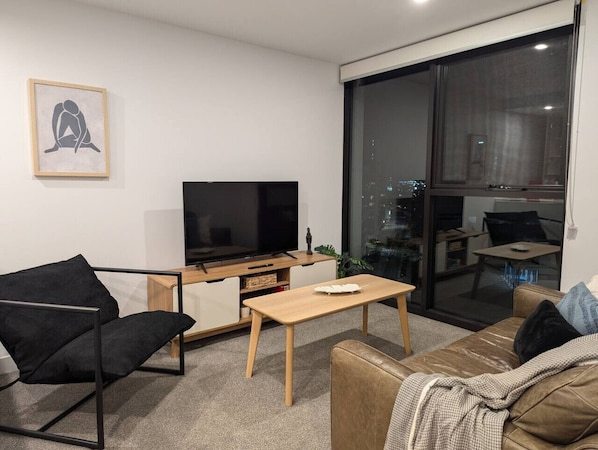 Un salon moderne avec un téléviseur à écran plat, une table basse en bois, un fauteuil noir et un canapé marron.