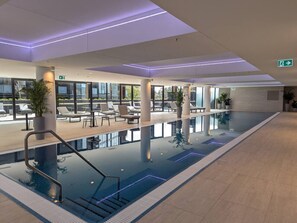 Une piscine intérieure moderne, avec une eau cristalline, entourée de chaises longues et de plantes en pot.