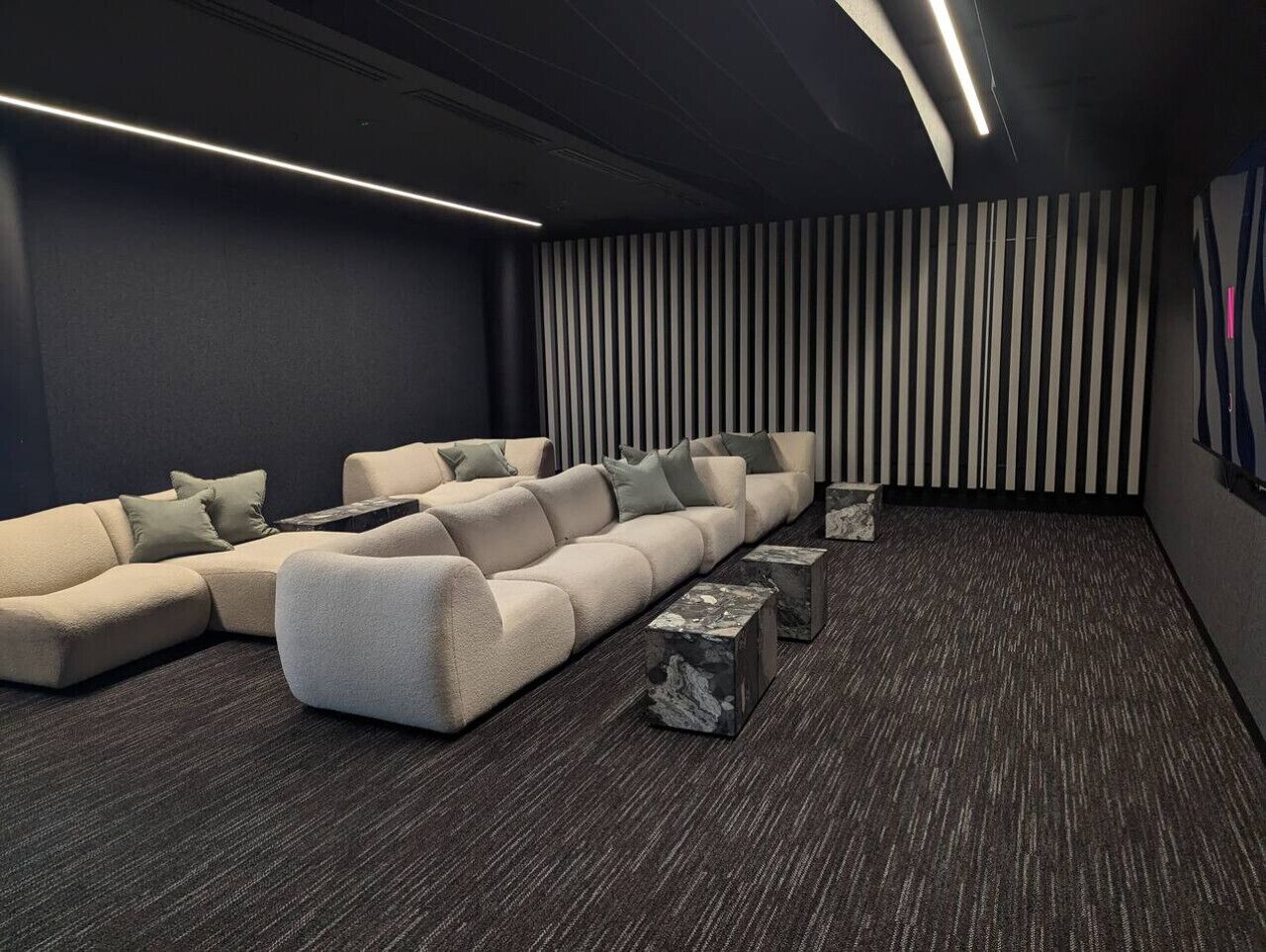 Ein moderner Heimkino-Raum mit einer Eckcouch, einem kleinen Couchtisch und einer gestreiften Wand.