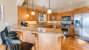 A modern kitchen with granite countertops, wooden cabinets, stainless steel appliances, and pendant lighting. - Moose Run Lodge – Slope-Side Luxury Retreat at Whitefish Mountain (Whitefish)