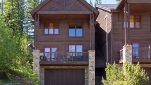 A two-story log cabin with a stone foundation, a covered front porch, and a garage. - Moose Run Lodge – Slope-Side Luxury Retreat at Whitefish Mountain (Whitefish)