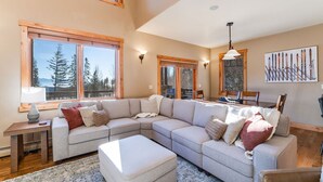 A spacious living room with a large L-shaped sectional sofa, a dining table, and a fireplace. - Moose Run Lodge – Slope-Side Luxury Retreat at Whitefish Mountain (Whitefish)