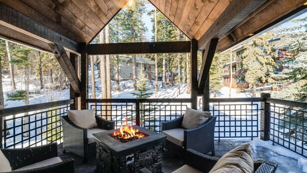 A covered outdoor seating area with a fire feature, wicker furniture, and a view of a snowy landscape. - Moose Run Lodge – Slope-Side Luxury Retreat at Whitefish Mountain (Whitefish)