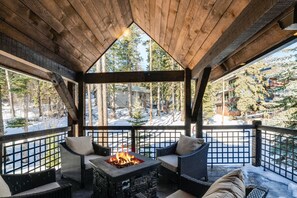 Un espacio exterior cubierto con zona de estar, chimenea, muebles de mimbre y vista a un paisaje nevado.