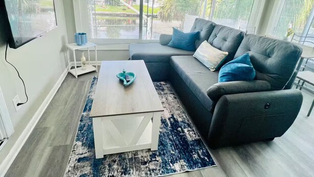 A modern living room with a grey sectional sofa, a coffee table, and a TV mounted on the wall.