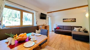 Een moderne woonkamer met een houten eettafel gedekt voor twee personen, een bank en een televisie aan de muur.