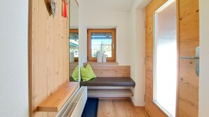 Een smalle gang met houten wanden, een bank met groene kussens, een radiator en een raam met uitzicht op buiten.