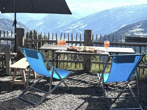 A wooden table with two blue chairs, a black umbrella, and a glass of drink.