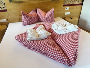 A neatly made bed with checkered bedding, pillows, and towels arranged for a guest.