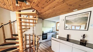Una cuina moderna amb armaris blancs, una escala espiraltra de fusta i un ampli quadre paisatge a la paret.