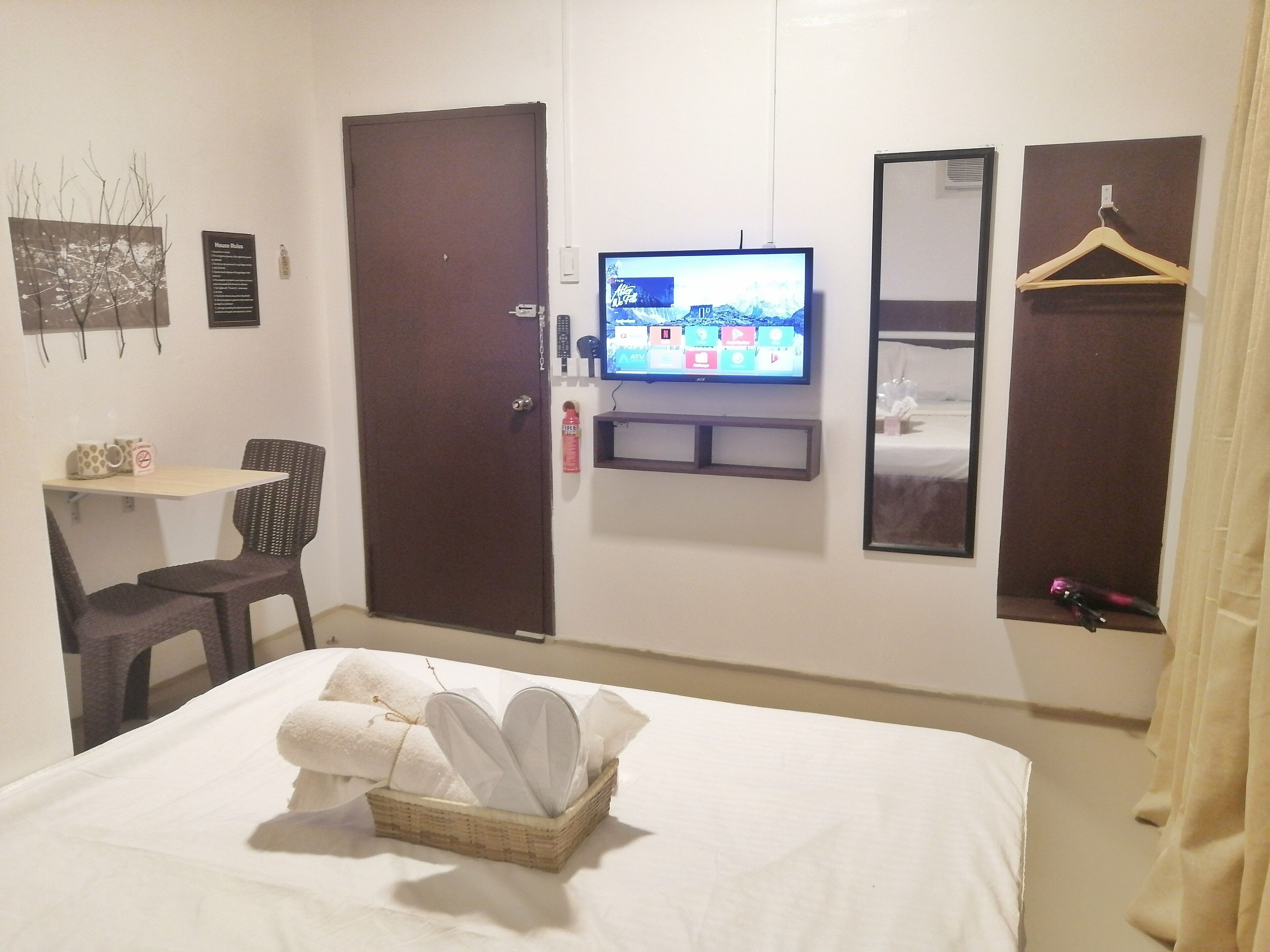 Habitación de hotel con cama, televisor en la pared, una mesita con silla y armario.