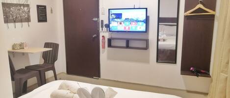 A hotel room with a bed, a TV on the wall, a small table with a chair, and a wardrobe.