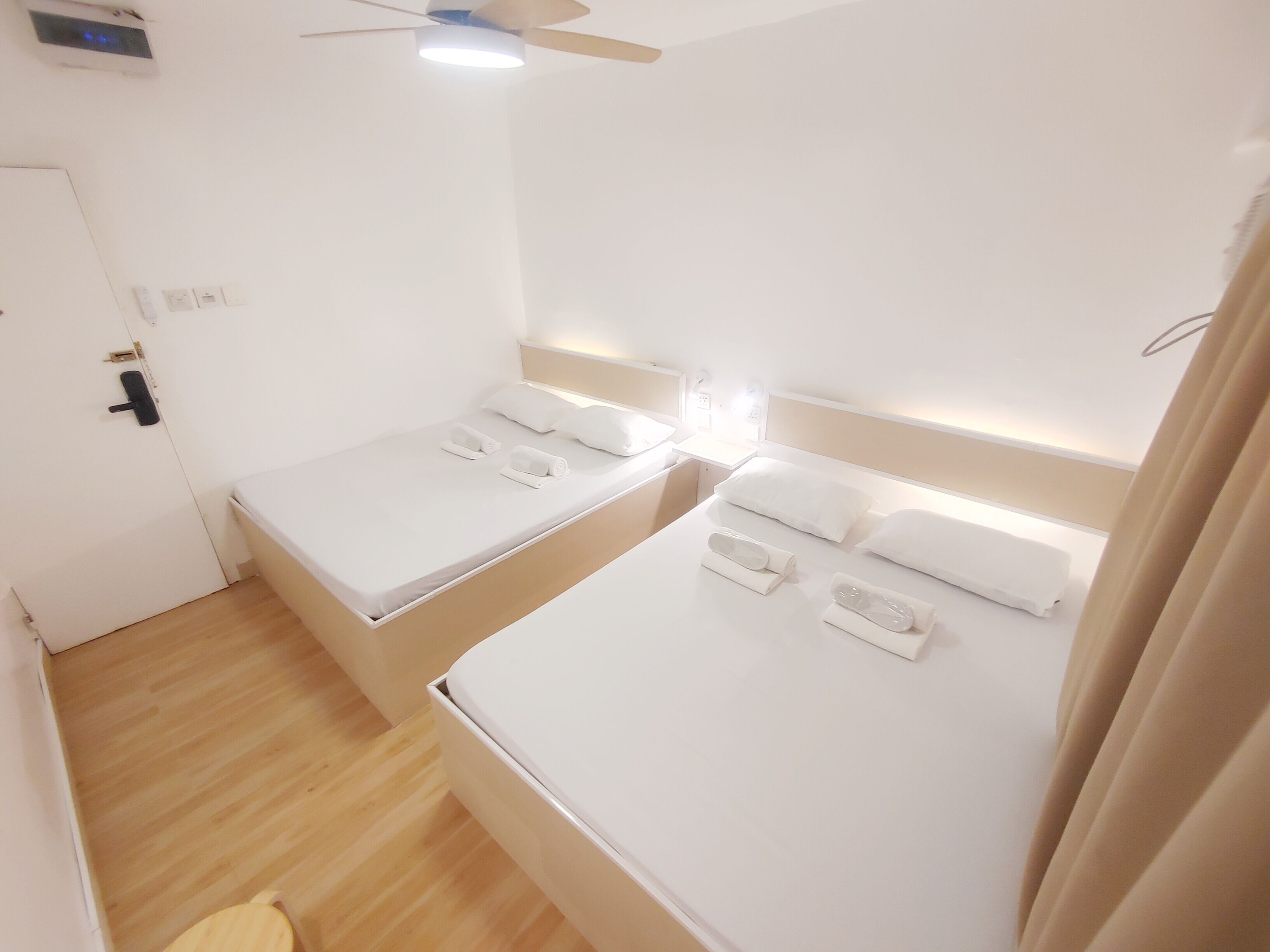 A hotel room with two single beds, a ceiling fan, a TV, and a door with a handle.
