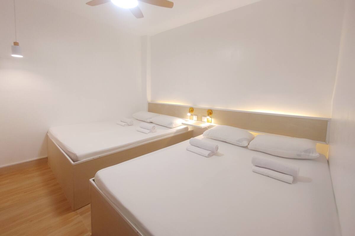 Ein Hotelzimmer mit zwei Einzelbetten, einem Deckenventilator, einem Nachttisch mit Lampe und einer Wandleuchte.