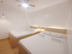 Ein Hotelzimmer mit zwei Einzelbetten, einem Deckenventilator, einem Nachttisch mit Lampe und einer Wandleuchte.