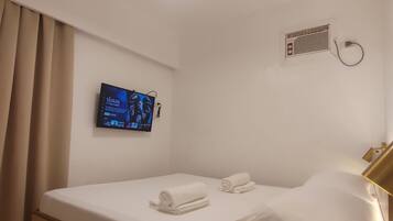 Una habitación de hotel con cama, ventilador de techo, televisor montado en la pared y aire acondicionado de pared.