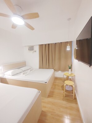 Habitació d'hotel moderna amb un llit gran, un ventilador de sostre, una televisió i una taula petita amb una planta.