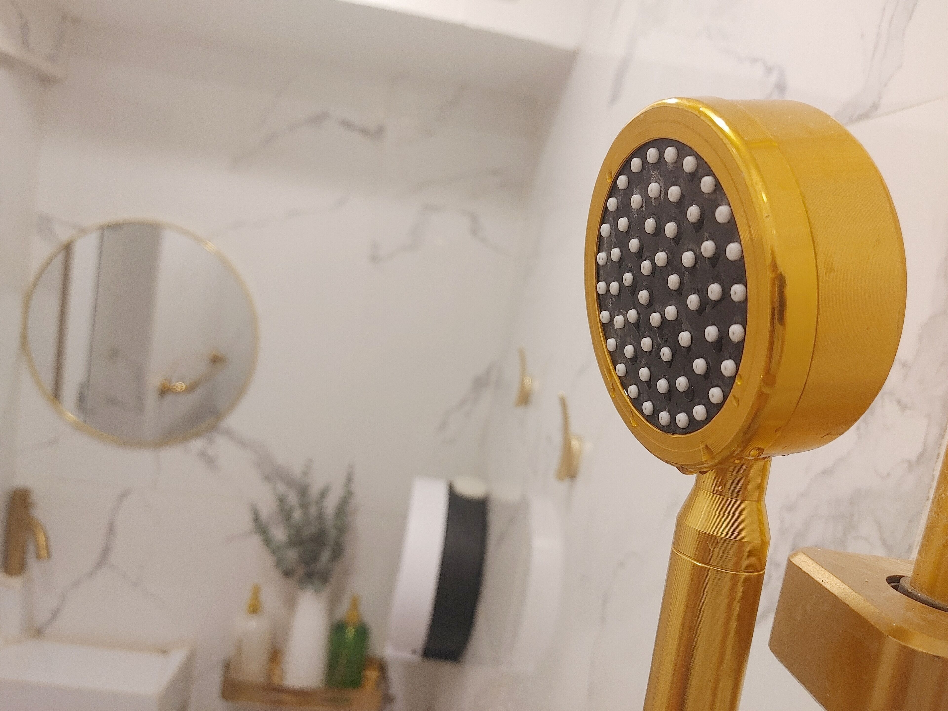 Une salle de bain avec une pomme de douche dorée, un miroir rond et un mur en marbre.