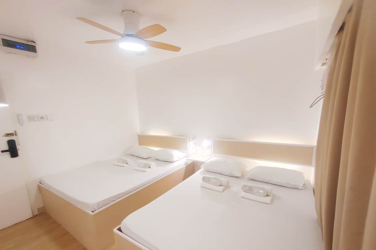 Ein Hotelzimmer mit zwei Einzelbetten, einem Deckenventilator und einem kleinen Fenster.
