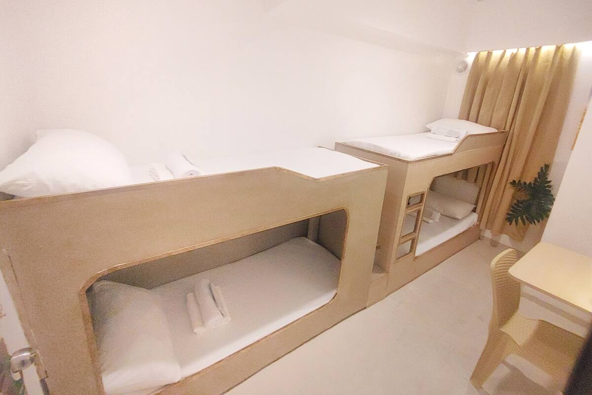 Ein Schlafraum mit Etagenbetten, Schreibtisch, Stuhl, einer Pflanze und einem Fenster mit Vorhängen.