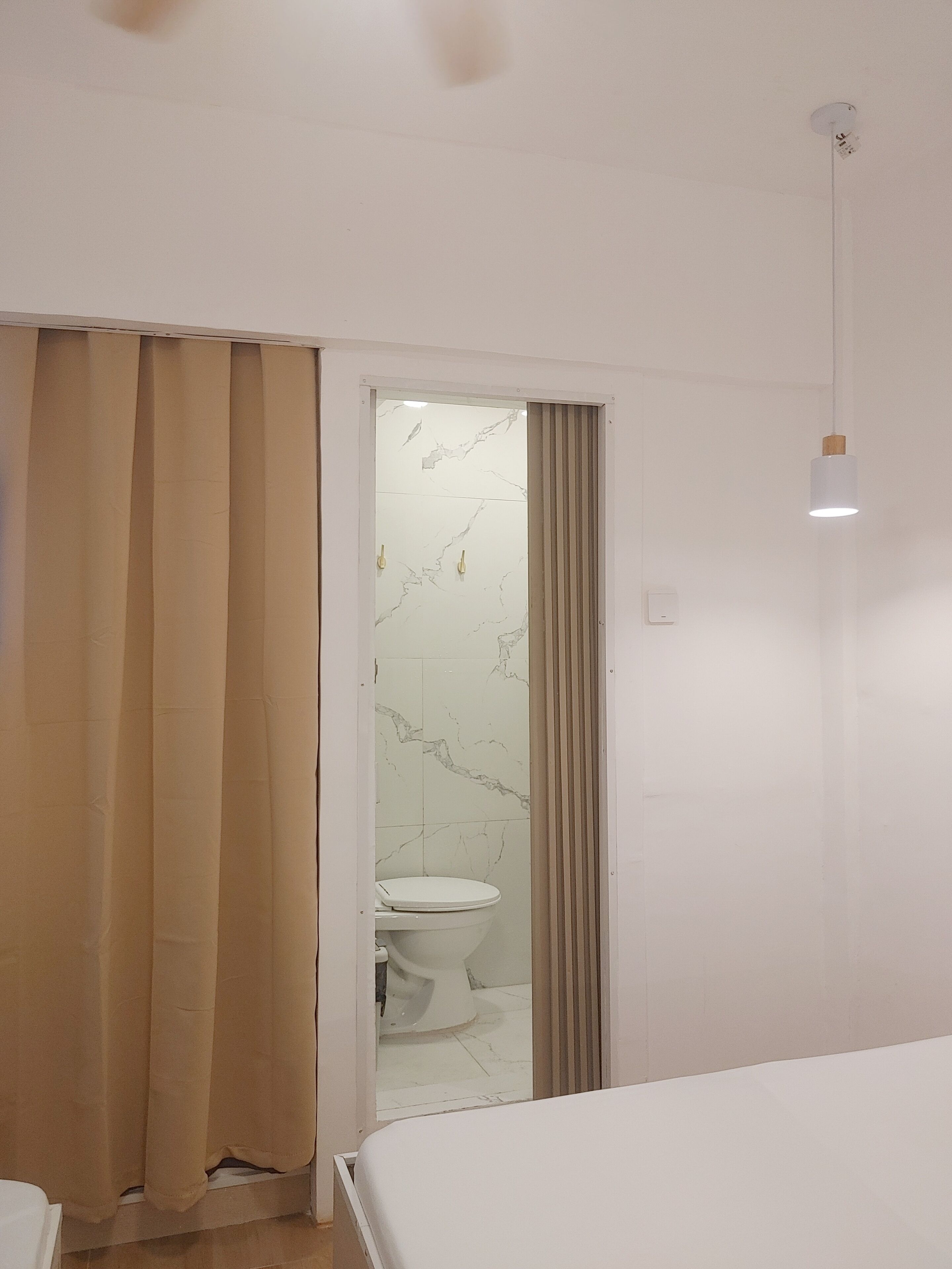 A hotel room with a bed, a bathroom with a toilet and a shower, and a curtain.