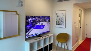 Een woonkamer met een flatscreen televisie aan een witte tv-meubel, een zwart-wit foto in een lijst aan de muur, en een gele fauteuil.