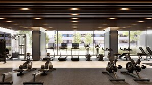 Een moderne sportschool met diverse trainingsapparaten, grote ramen en uitzicht op gebouwen.