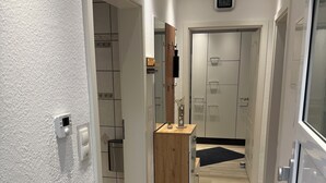 A modern hallway with white walls, a wooden door, and a mirror. - Cozy 2 X room, kitchen bathroom apartment in the Karl Marx Siedlung in Worms 1st floor (Worms)