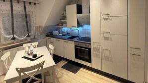 A modern kitchen with white cabinetry, a built-in oven, and a dining area with a white table and chairs. - Cozy 2 X room, kitchen bathroom apartment in the Karl Marx Siedlung in Worms 1st floor (Worms)