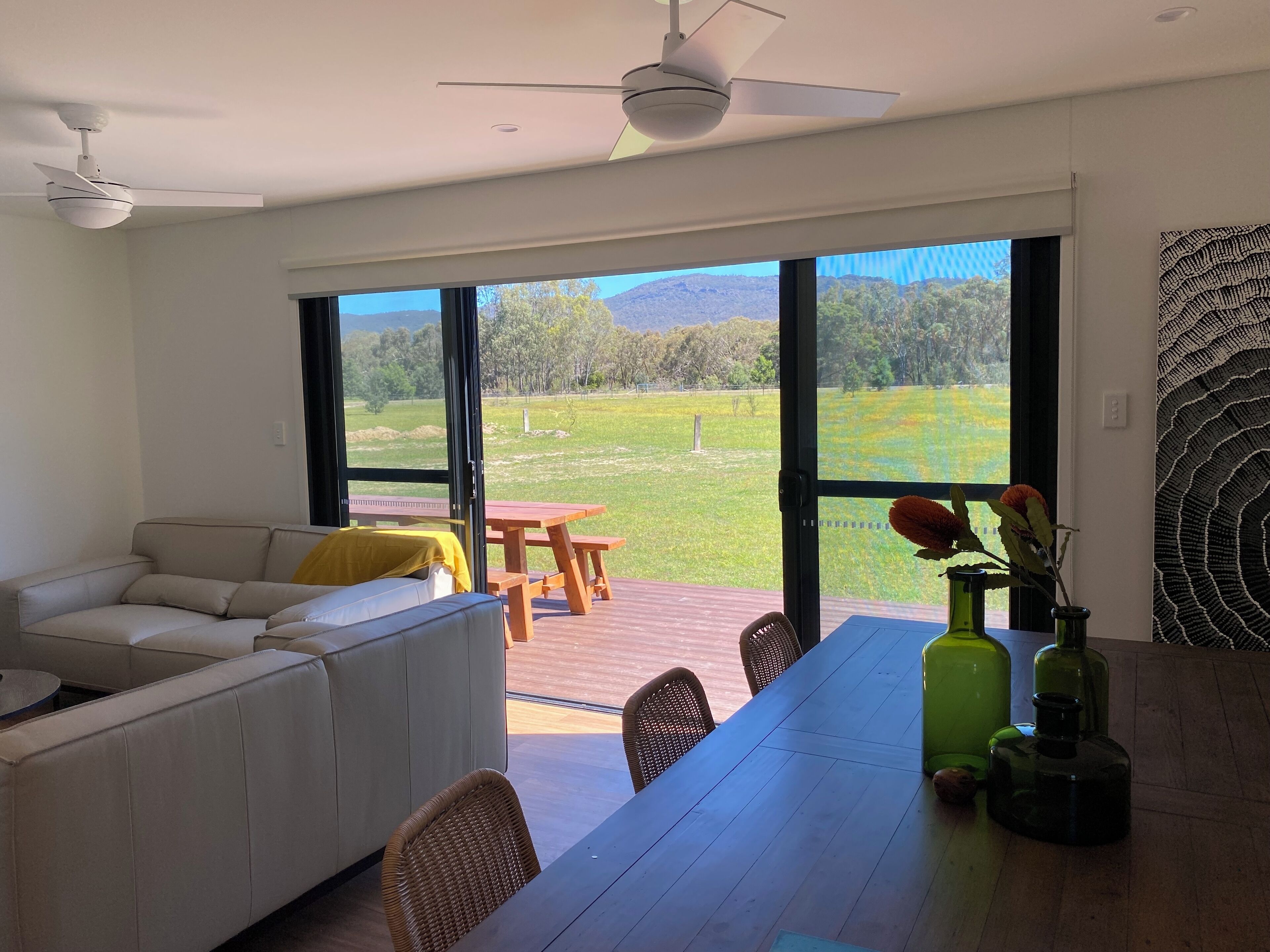 Una sala moderna con sofá, mesa de comedor, sillas y vistas a un campo verde a través de amplias ventanas.