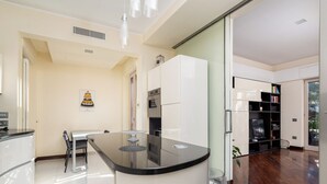 A modern kitchen with a central island, a dining area with a table and chairs, and a bookshelf with books. - Pine House (Sorrento)