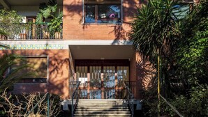 A set of concrete stairs leading to a building entrance with a metal railing and a window with flowers. - Pine House (Sorrento)