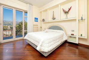 A bedroom with a large bed, a balcony with a view of the mountains, and a small shelf with decorative items. - Pine House (Sorrento)