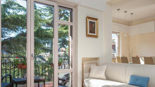 A living room with a white sofa, a glass door leading to an outdoor area with a patio and chairs, and a painting on the wall. - Pine House (Sorrento)