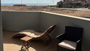 A balcony with two lounge chairs and a small table, overlooking a beach and a residential area. - Joli Beach House - T1 Beautiful and Authentic Island Living (Sal)