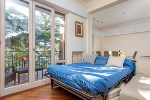 Un dormitorio con cama, un radiador, una ventana y un balcón con sillas.