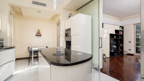 Een moderne keuken met een centraal eiland, een eethoek met een tafel en stoelen, en een zithoek met een televisie en boekenkasten.