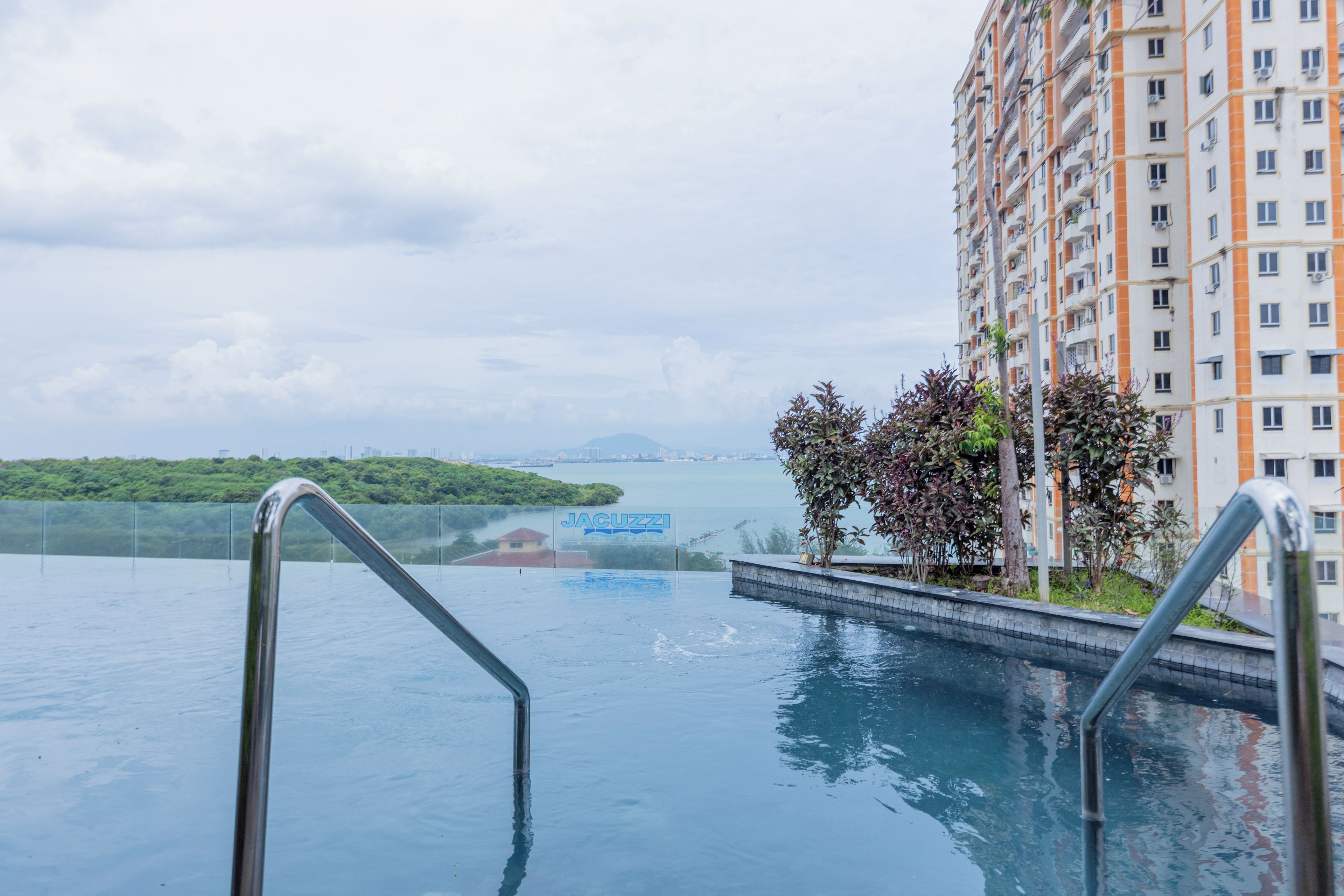 A swimming pool with metal railings, a sign for 'JACUZZI', and a high-rise building in the background.