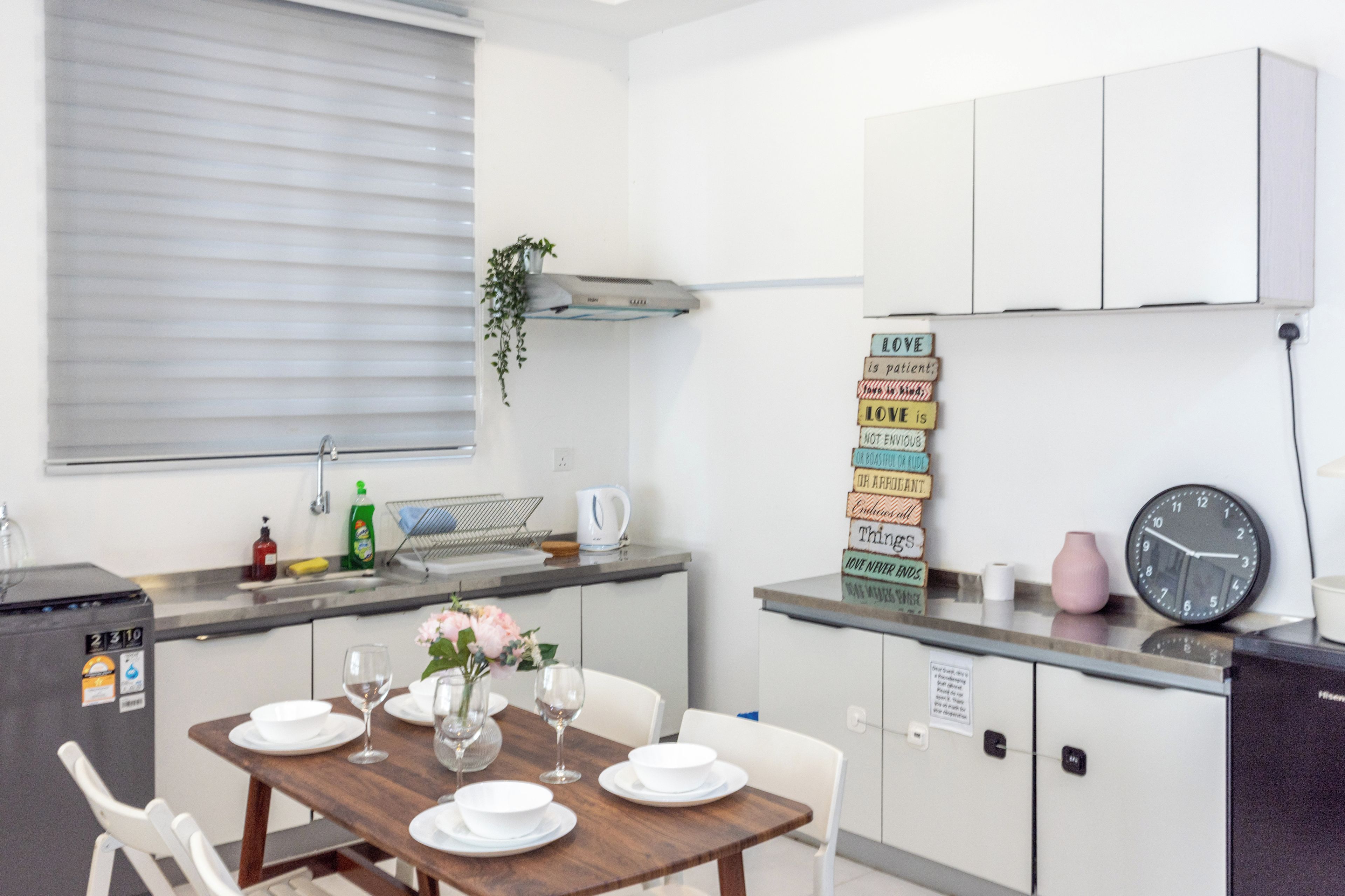 A compact kitchen with a dining table set for four, a clock, and a sign with positive affirmations.
