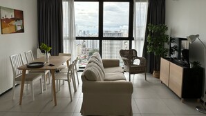 Un salon moderne comprenant un canapé, une table à manger, des chaises, un téléviseur et une grande fenêtre donnant sur la ville.