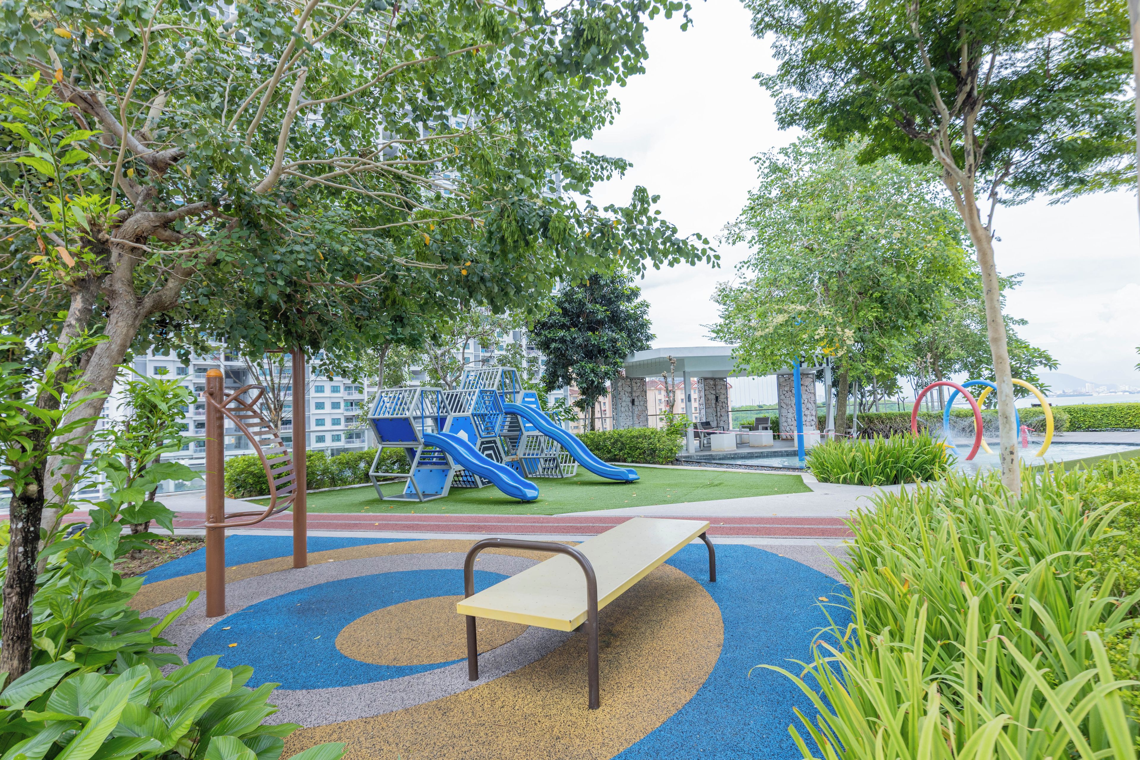 A playground with slides and climbing structures, surrounded by trees and a building in the background.
