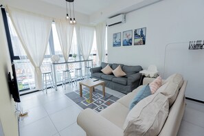 A modern living room with a grey sofa, a coffee table, and a dining area with a balcony. - Urban Suite Penang (George Town)