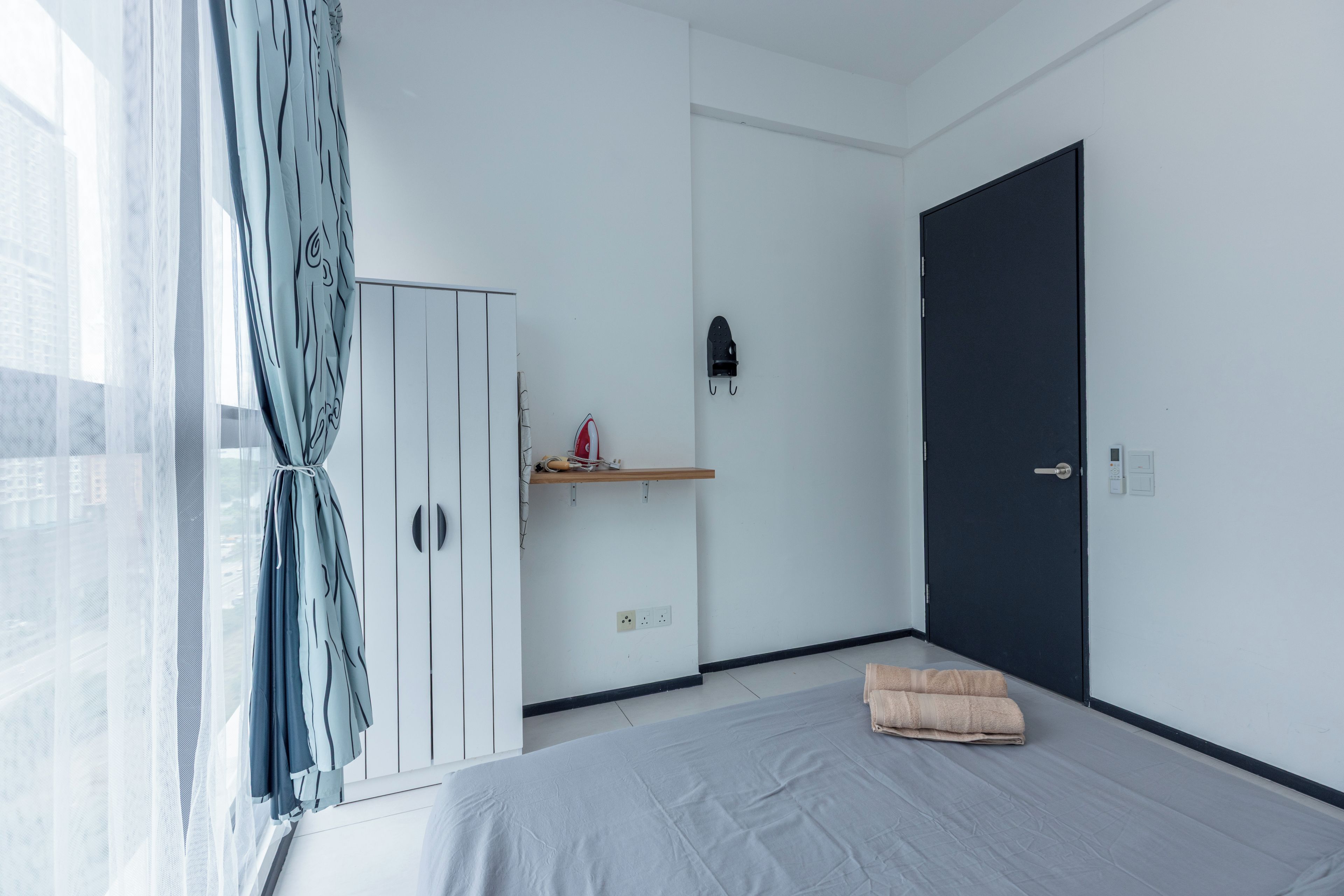 Quarto minimalista com cama, guarda-roupa, porta e janela com cortinas.