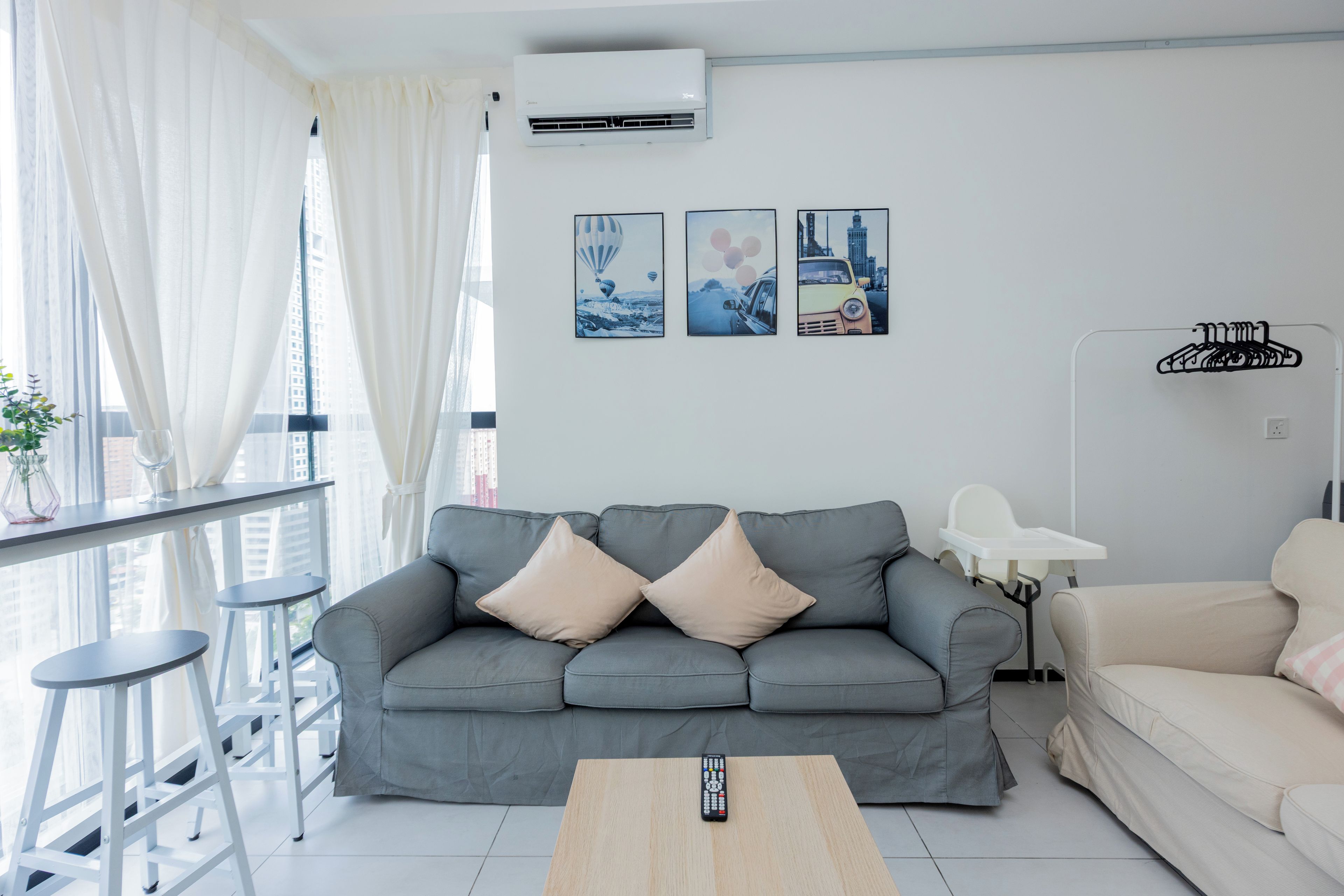 Ein modernes Wohnzimmer mit grauem Sofa, einem weißen Sessel, einem Couchtisch, einem Fernseher und einem Balkon mit Geländer.
