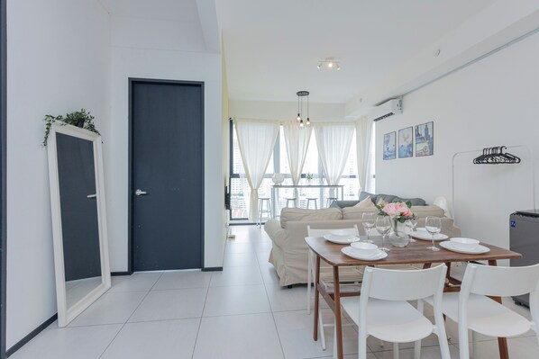 A modern dining area with a table set for four, white chairs, and a view of a cityscape through large windows.
