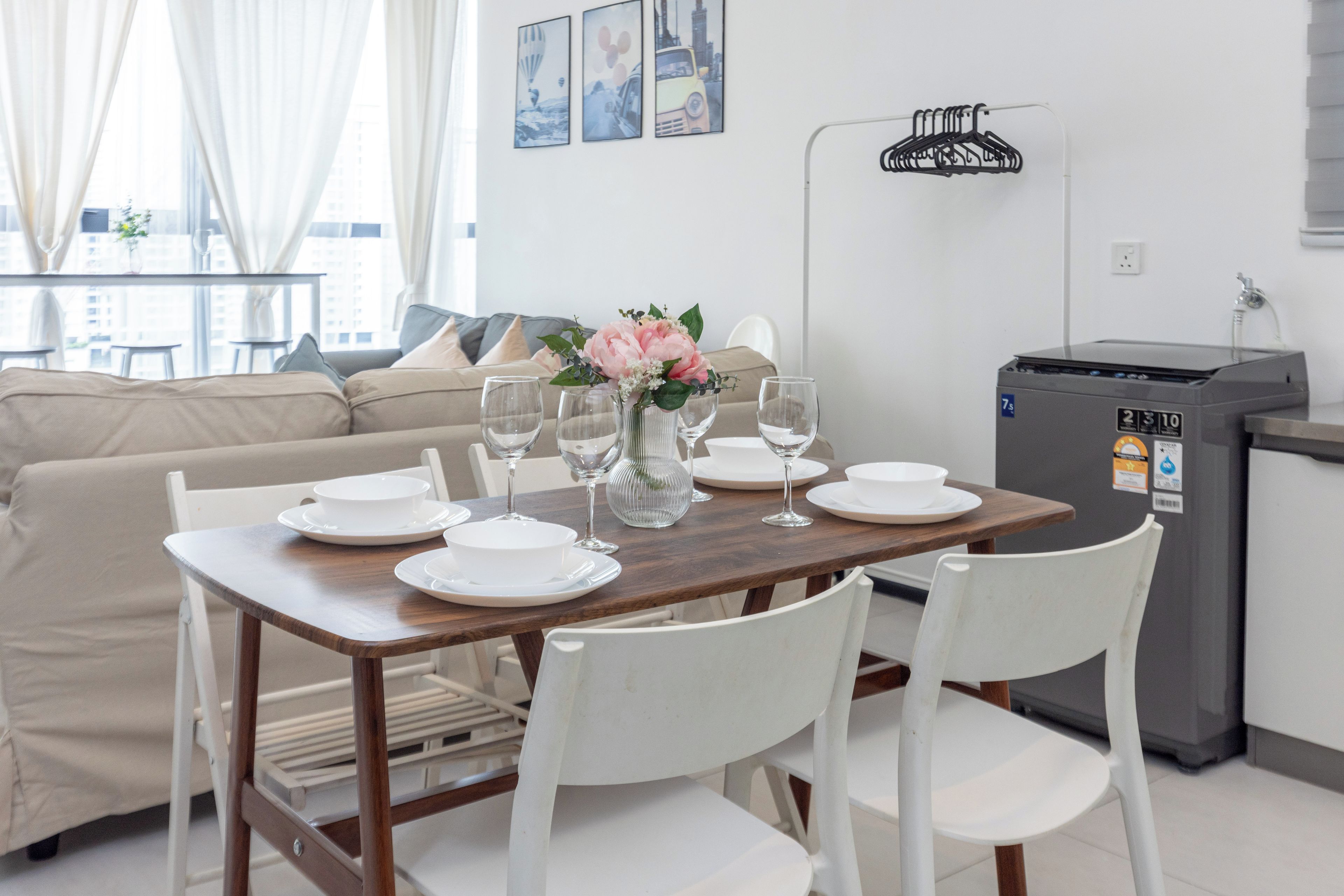 A dining area with a wooden table set for four, white chairs, and a vase with flowers.