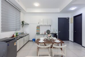 A compact kitchen with a dining area, a refrigerator, a sink, and a clock on the wall.
